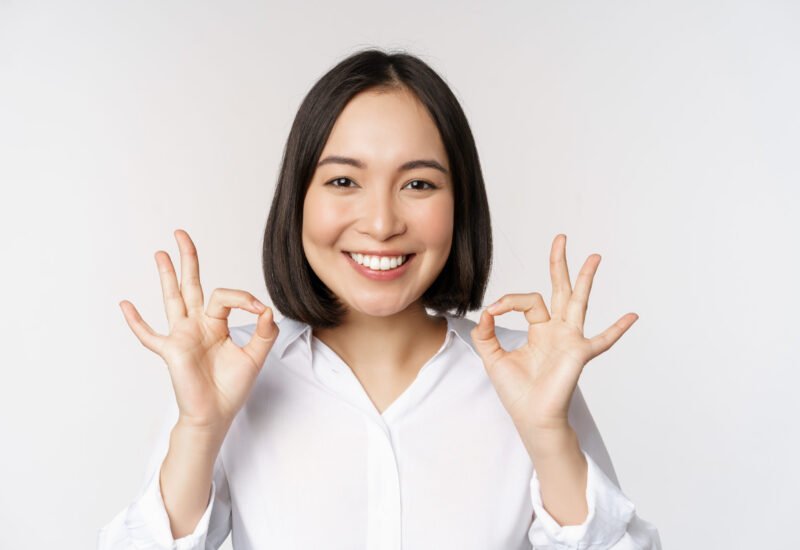 close up head portrait asian girl showing okay ok sign smiling satisfied recommending being pleased praise make compliment white background scaled